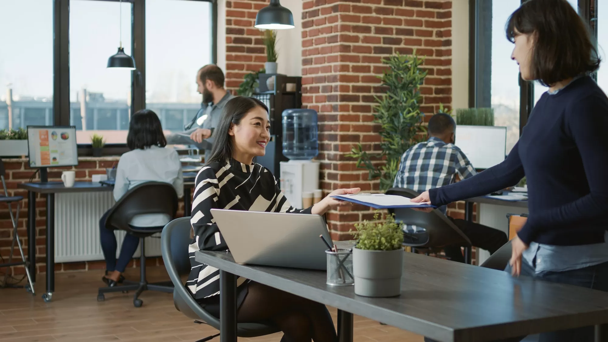 Colleagues collaborating and handing over documents in a modern open-plan office
