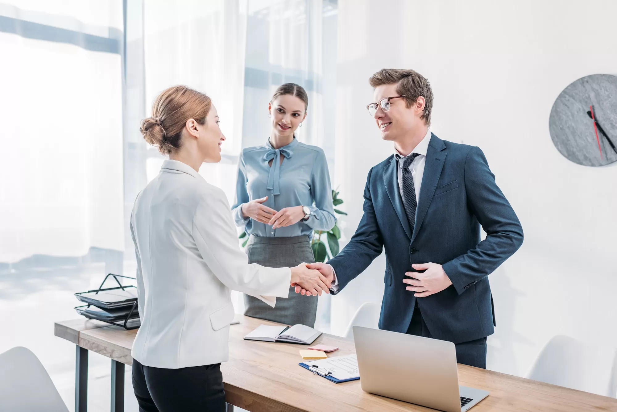A recruiter shaking hands with a candidate while a colleague looks on in a bright office