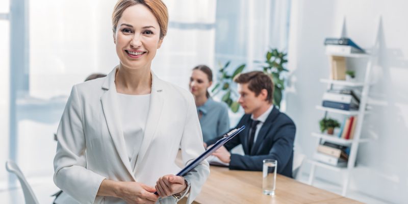 selective focus of cheerful recruiter standing with clipboard near coworkers